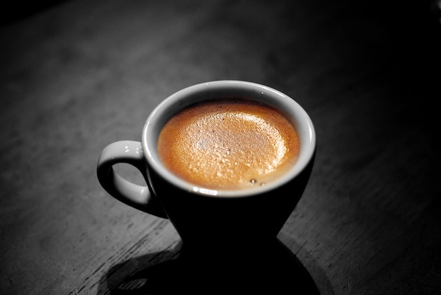 A black ceramic cup of espresso on a dark wooden tabletop