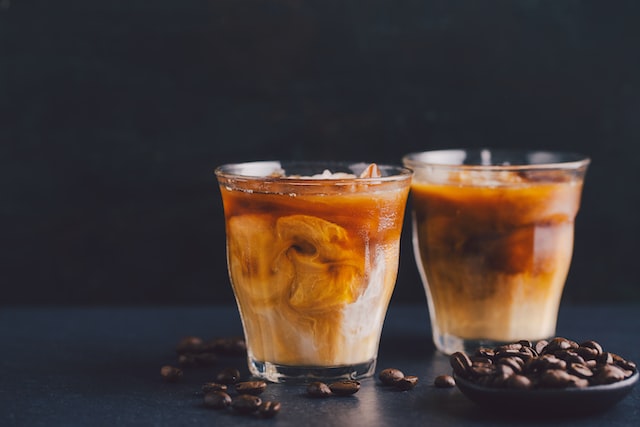 Two glasses of iced coffee with coffee beans on a dark tabletop