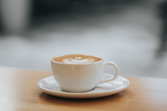 A white ceramic cup (with saucer) of cappuccino on a light wooden tabletop